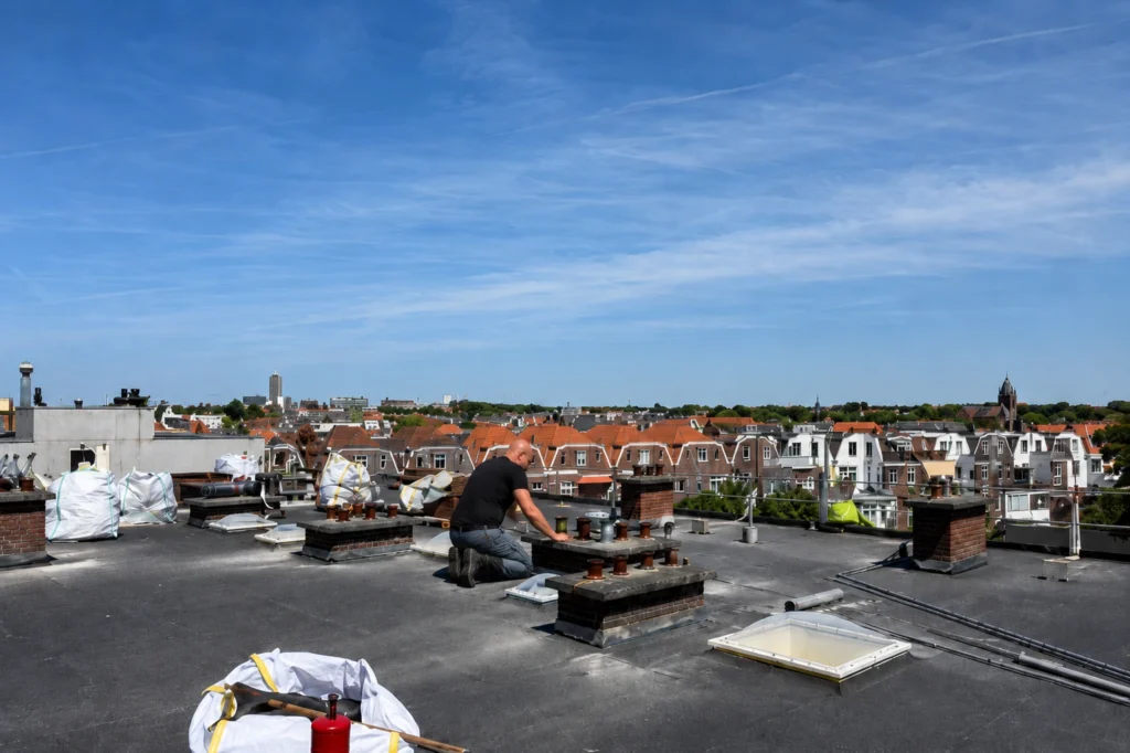 Dakdekker aan het werk op een plat dak in een woonwijk