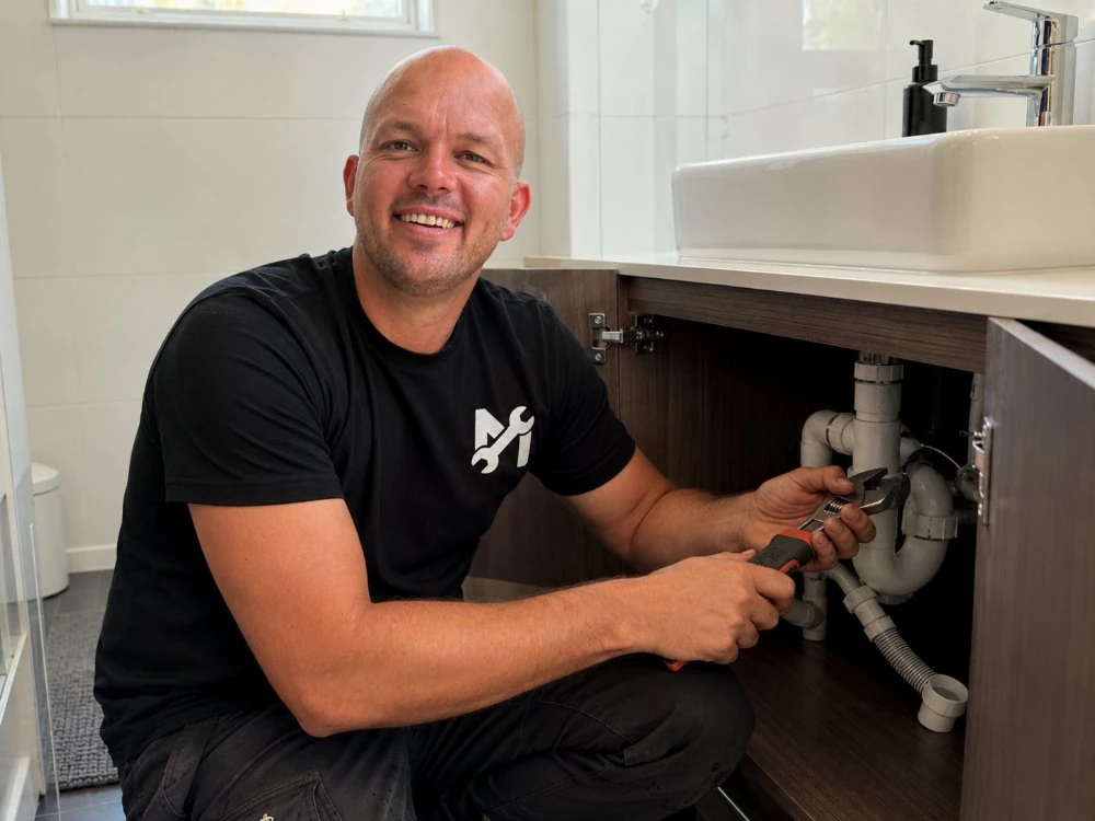 Lachende loodgieter werkt aan de afvoer onder een wastafel